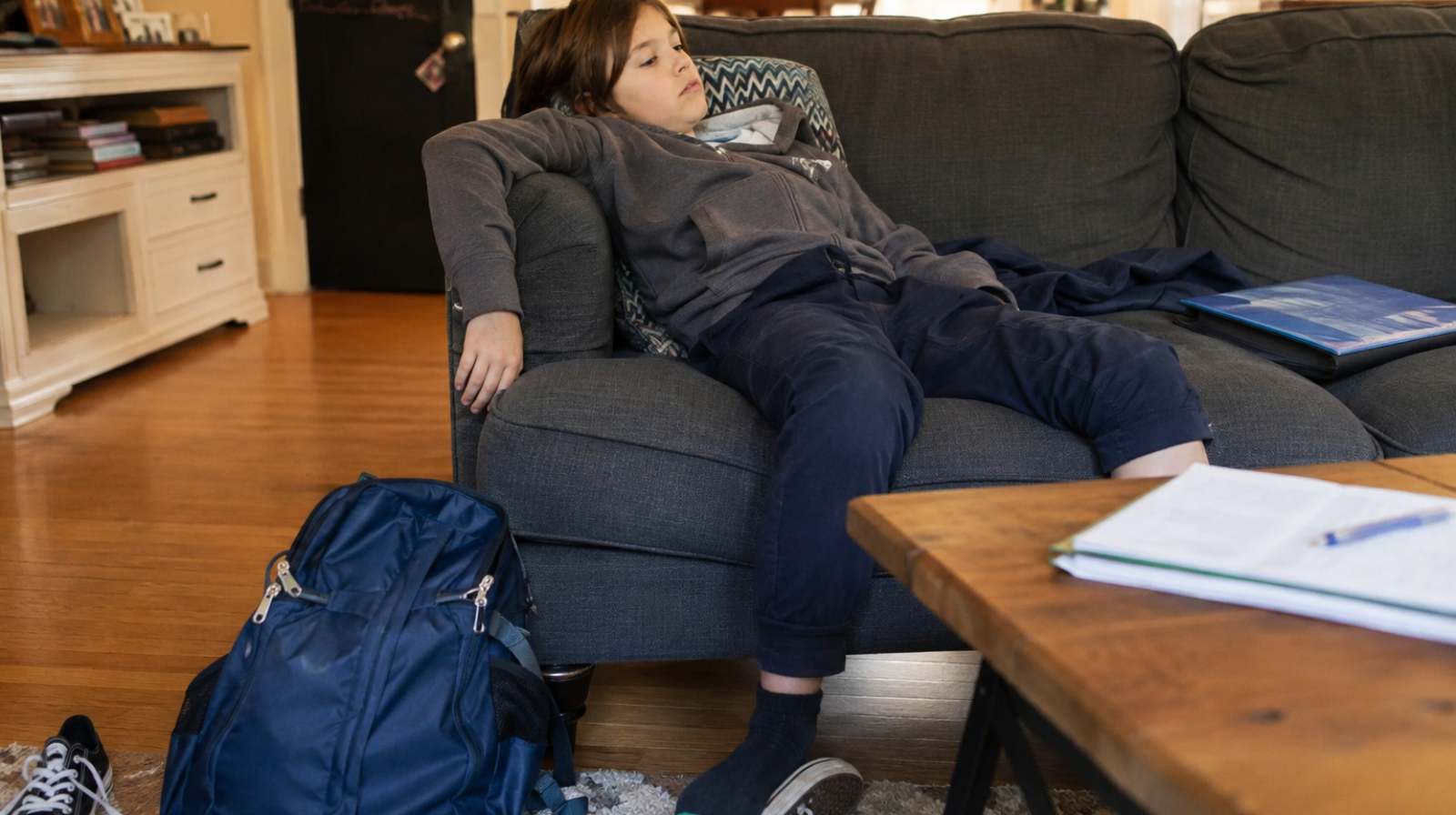Child with ADHD relaxing on the couch after school, with a backpack and homework nearby, illustrating the after-school crash.